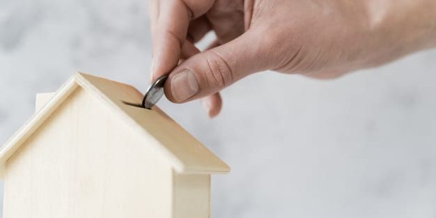 close-up-person-s-hand-inserting-coin-wooden-house-piggybank_23-2148038721